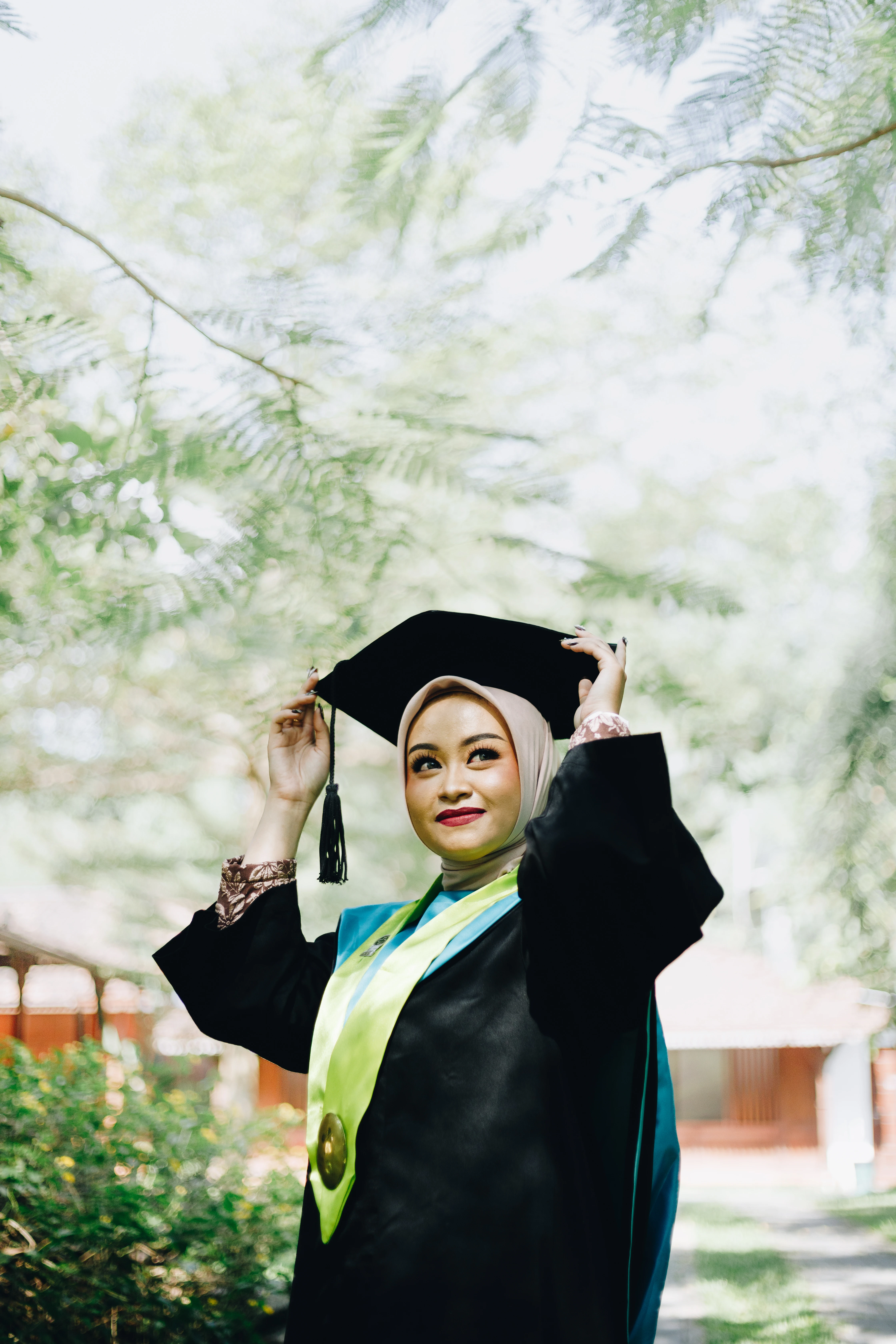 Foto wisuda outdoor mahasiswi UGM dengan toga hitam dan samir kuning di bawah sinar matahari hangat Bulaksumur Yogyakarta - Toga & Co.