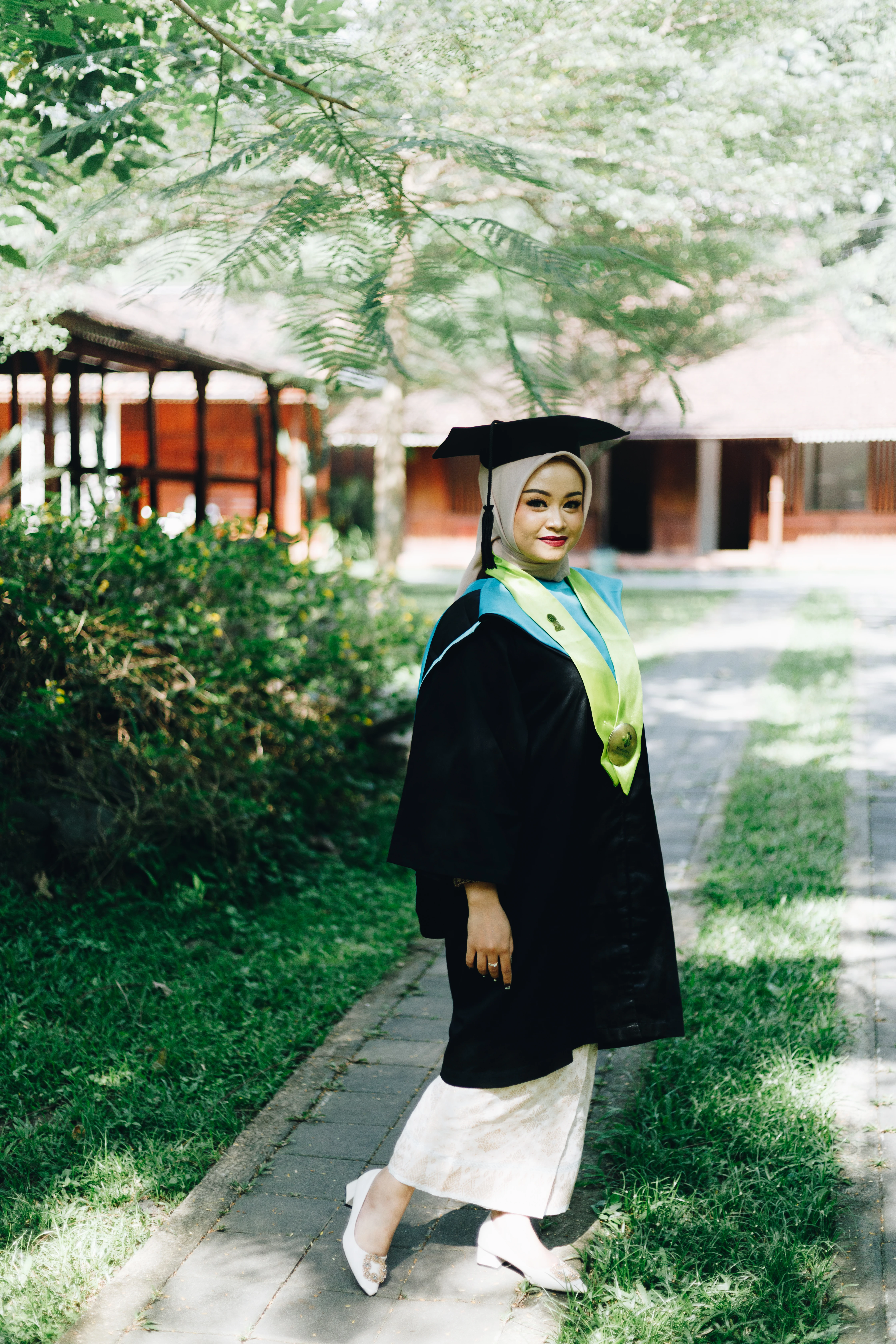 Potret wisuda personal mahasiswi tersenyum memegang buket bunga di halaman GSP UGM Yogyakarta bernuansa hangat alami - Toga & Co.